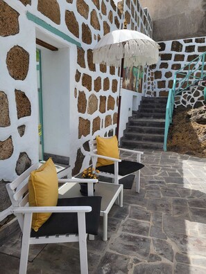 A stone-walled building with a staircase leading to a door. There are outdoor seating areas with chairs and cushions.