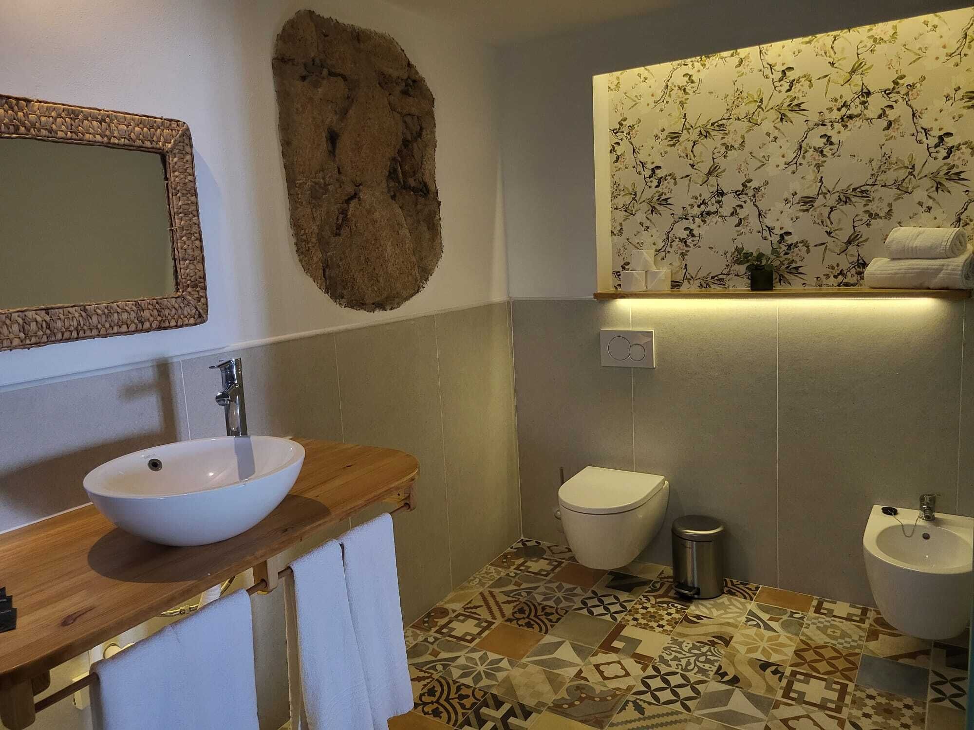 Et badeværelse med en trækommode, en hvid vask, et toilet og en bidét.