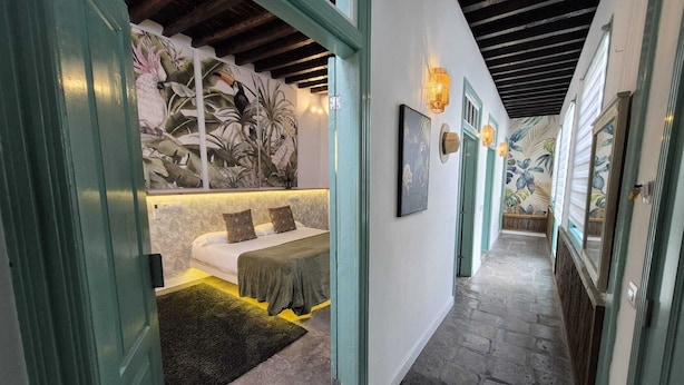 A hallway with a bed, a green door, and a wall with a tropical mural.