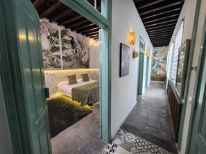 A hallway with a bed, a green door, and a wall with a tropical mural. - Hacienda de las Indias (Granadilla de Abona)
