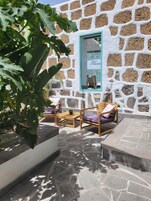 Un muro de piedra con una ventana, asientos al aire libre y una planta grande.