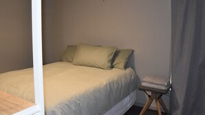 Et soveværelse med en seng, puder, et natbord og et gardin.