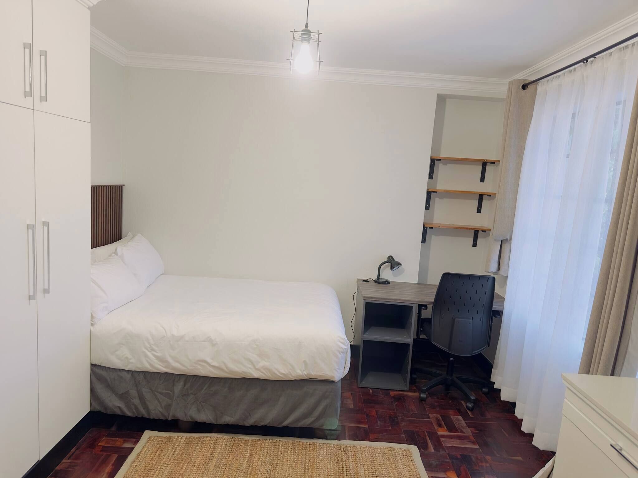 Un dormitorio con cama, escritorio, silla, armario y una lámpara colgante.