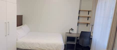 A bedroom with a bed, desk, chair, wardrobe, and a hanging light fixture.