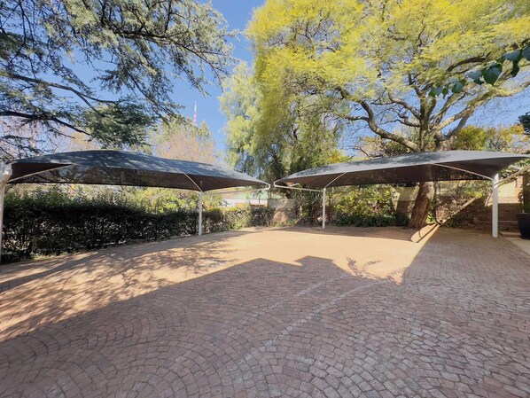 A paved outdoor area with two covered seating areas, surrounded by trees and a clear sky.