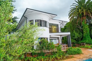 A modern two-story house with a curved roof, large windows, and a well-maintained garden with a pool.