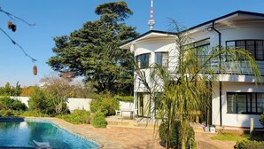 Ein zweigeschossiges Haus mit Schwimmbad, umgeben von viel Grün und blauem Himmel.
