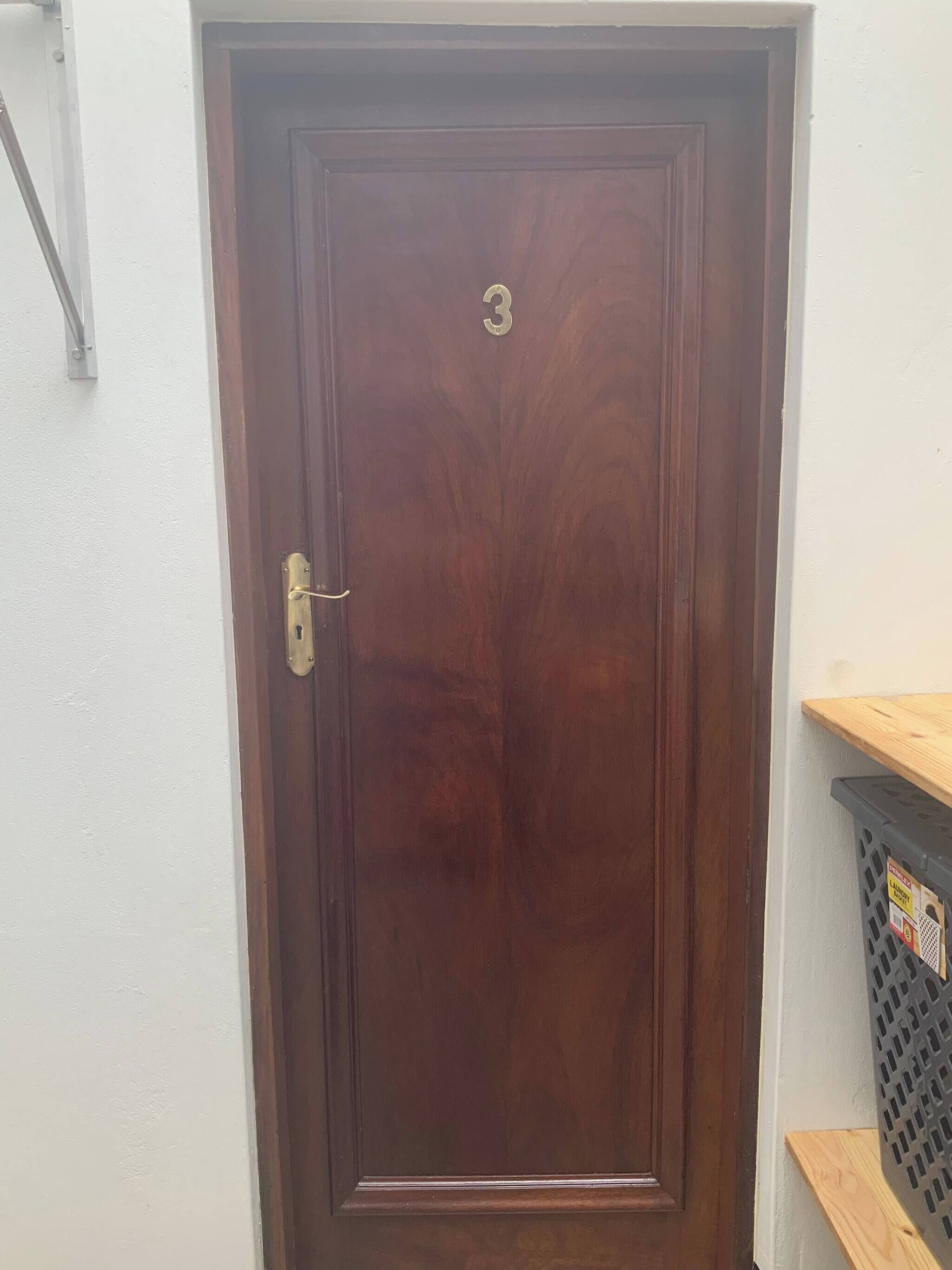 A closed wooden door with a brass handle and a small brass plate with the number '3' on it.