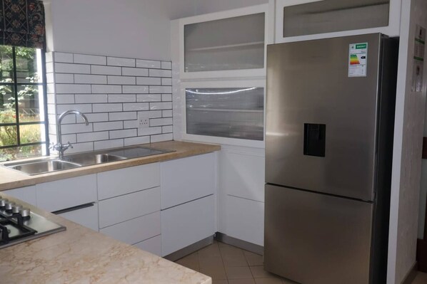 A kitchen with white cabinets, a stainless steel refrigerator, a window, and a sink.