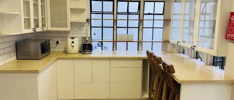 A kitchen with white cabinets, a microwave, a coffee maker, and a window with blinds.