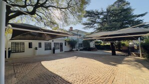 Un patio con suelo empedrado, zonas de estar cubiertas y un edificio blanco con ventanas y puertas.