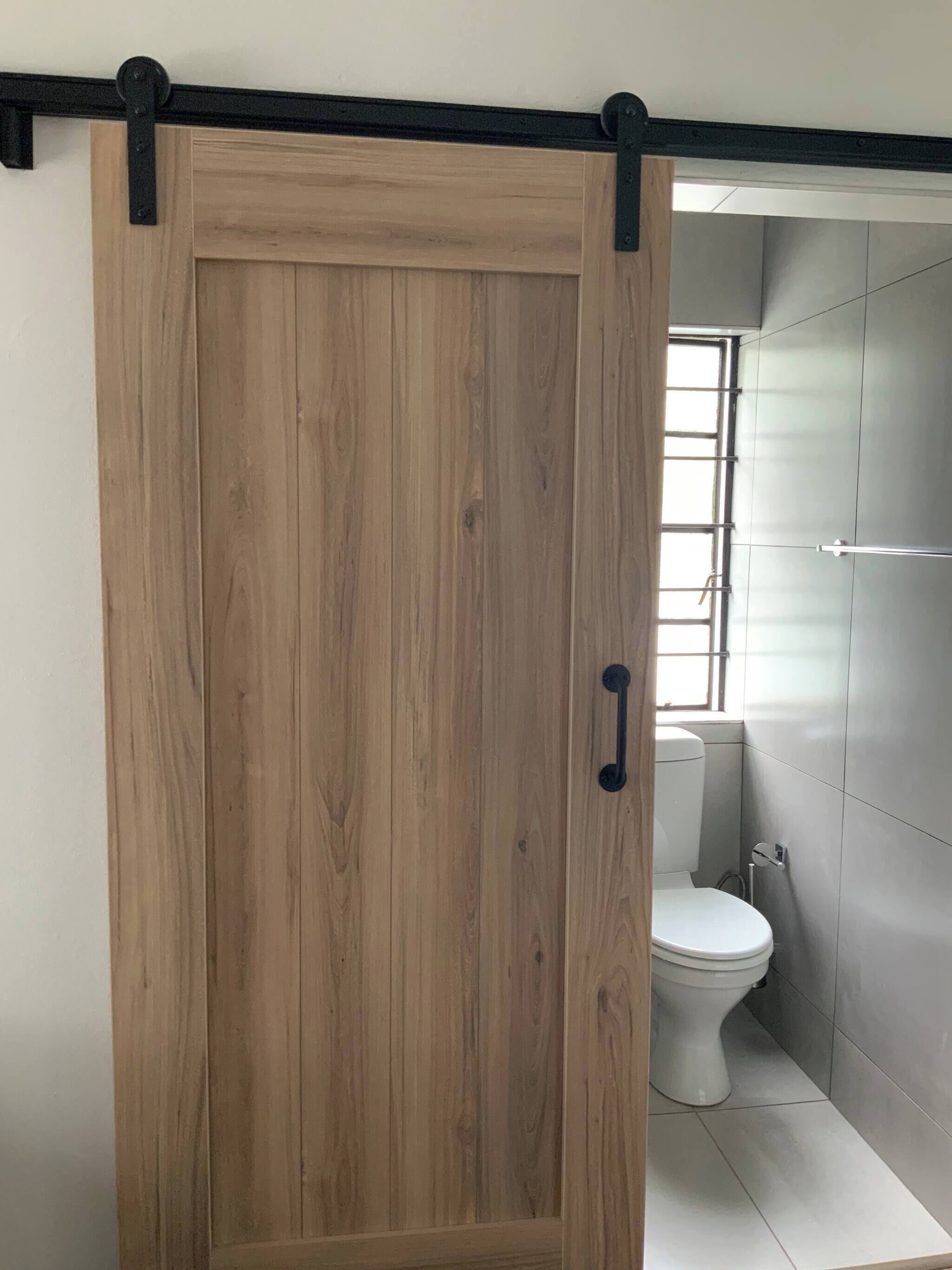 A wooden sliding door in a bathroom with a toilet and a window.