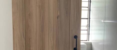 A wooden sliding door in a bathroom with a toilet and a window.