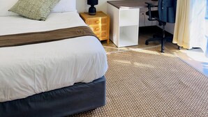 Habitación de hotel con cama, escritorio, silla, mesita de noche y ventana con cortinas.