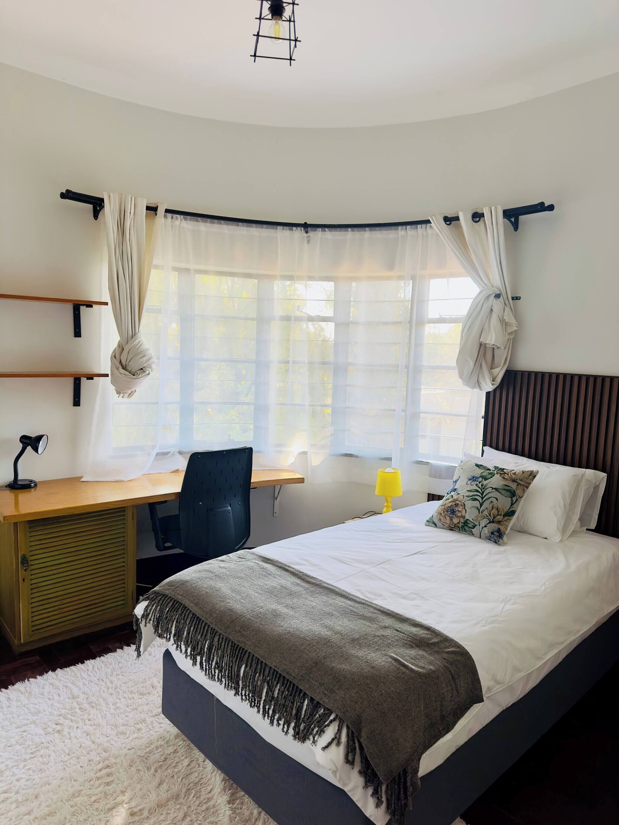 Un dormitorio con cama, escritorio, silla y ventana con cortinas.