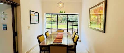 A conference room with a long table, chairs, a rug, a chandelier, and large windows with a view of greenery.