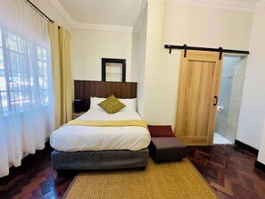 Habitación de hotel con cama, mesita de noche, espejo, puerta y vistas al exterior.