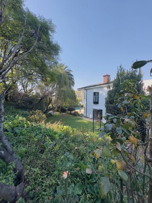 Un edificio blanco con puerta negra, rodeado de abundante vegetación y árboles.