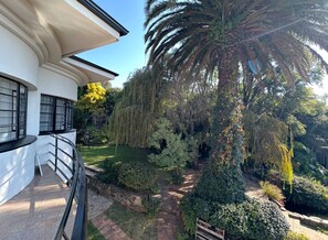 Un edificio moderno con un balcón curvo, una palmera y un jardín bien cuidado con diversos arbustos y un camino.