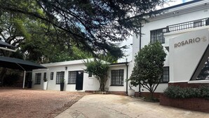 A building with a sign reading 'ROSARIO'S' and a paved courtyard with a brick pathway. - Room-single Room With Shared Bathroom 1 (Johannesburg)