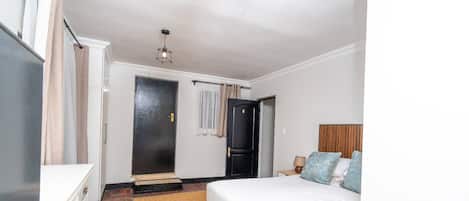 Un dormitorio con cama, mesita de noche, puerta y lámpara colgante.