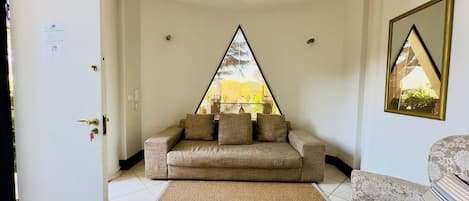 A room with a sofa, a patterned rug, a door, and a window with a view of trees.