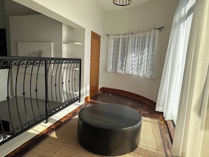 A hallway with a round ottoman, a black metal railing, and a door.