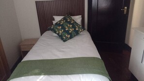 A single bed with a green blanket, white bedding, and a floral pillow.