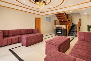 A spacious lobby with a large red sofa, a matching ottoman, and a chandelier. - Collection O Shalimar Garden Srinagar (Srinagar)