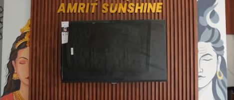 Un televisor empotrado con diseño de panel de madera, un reloj encima y el texto 'AMRIT SUNSHINE' debajo.