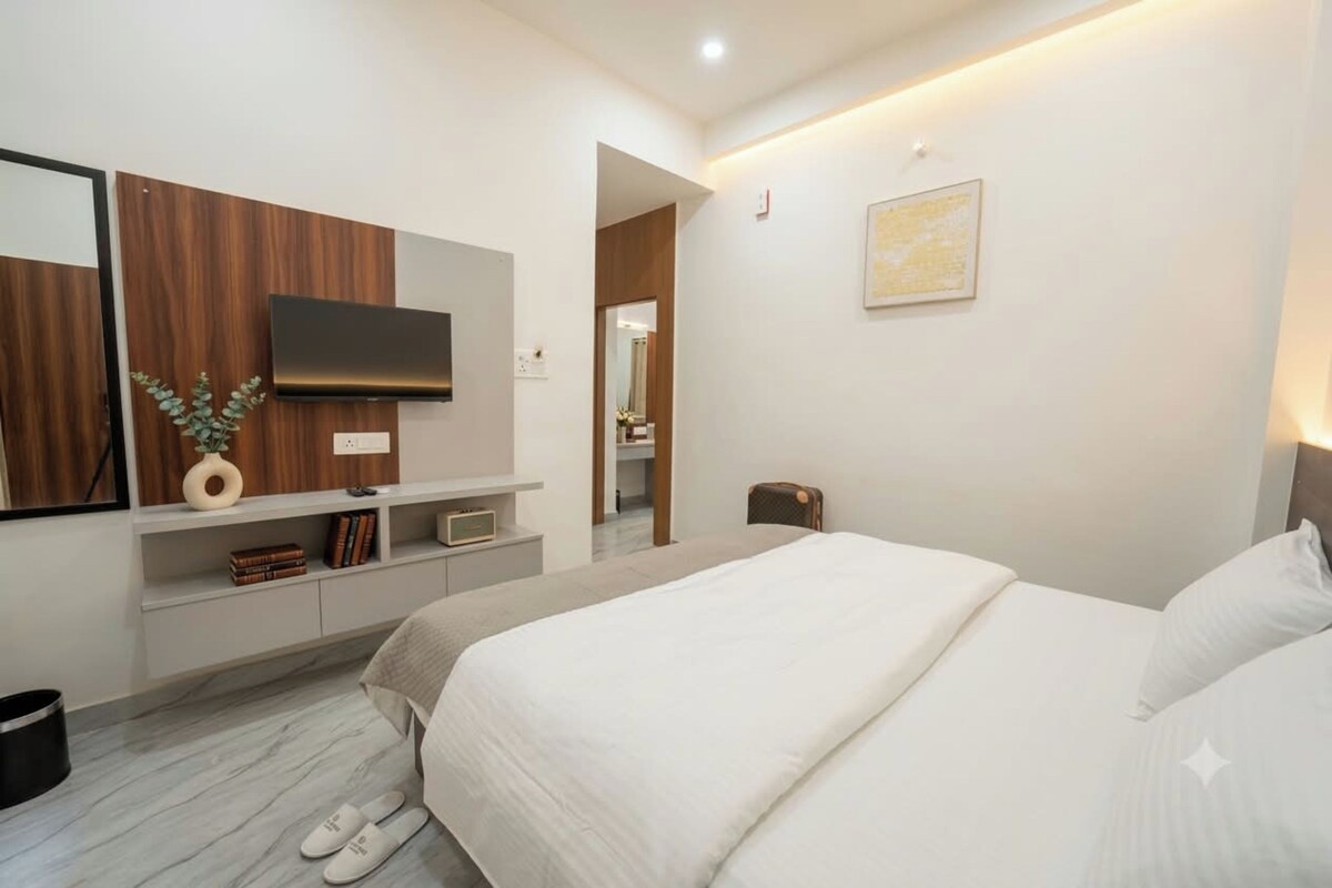 A modern hotel room with a large bed, a TV mounted on the wall, a small desk, and a mirror.