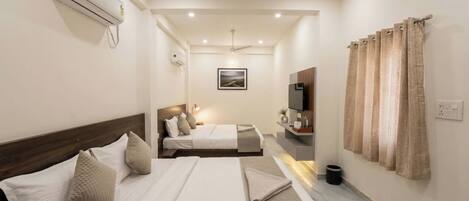 Una habitación de hotel con una cama, un escritorio, una silla, un televisor y un ventanal con cortinas.