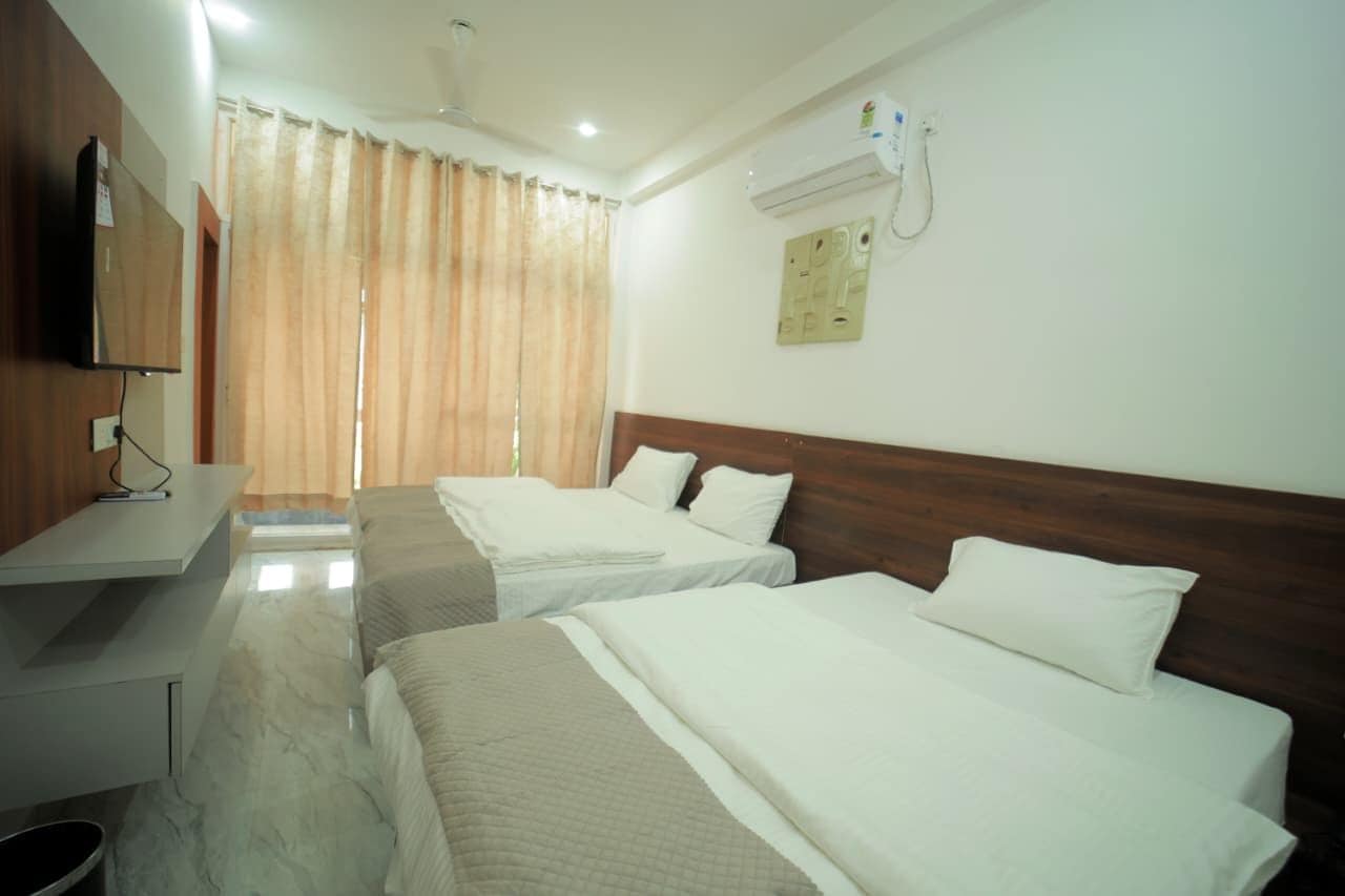 A hotel room with two beds, a desk, a television, and an air conditioning unit.