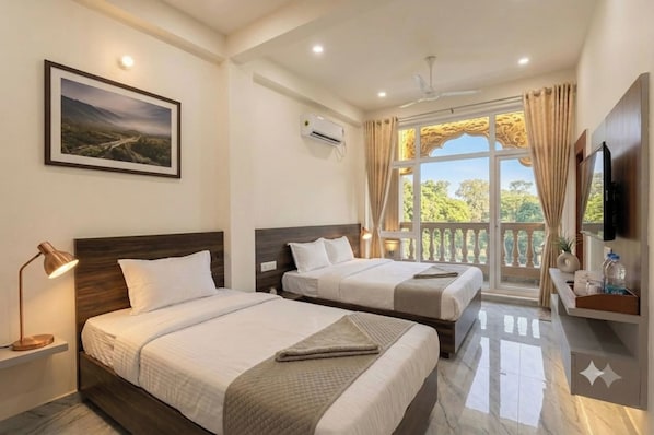 Habitación de hotel con dos camas, un televisor montado, un cuadro en la pared y un balcón con cortinas.