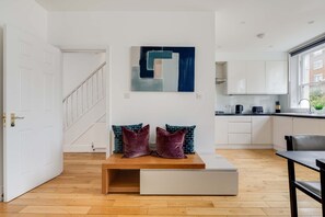 A modern kitchen with white cabinets, a black countertop, and a window. - Cozy 3BR Flat By Hyde Park (London)