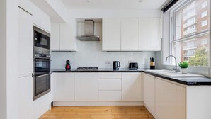 Een moderne keuken met witte kasten, een zwart aanrecht en een houten vloer.