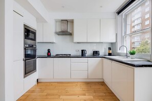 A modern kitchen with white cabinetry, a black countertop, and a wooden floor. - Cozy 3BR Flat By Hyde Park (London)