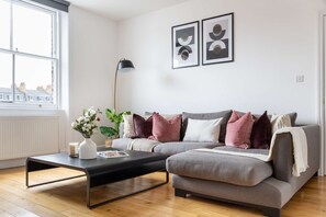 A modern living room with a grey sofa, a black coffee table, and a floor lamp. There are two framed abstract artworks on the wall. - Cozy 3BR Flat By Hyde Park (London)