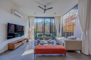 Una sala de estar moderna con televisor de pantalla plana, sofá, reposapiés y ventilador de techo.