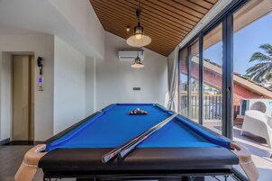 Una mesa de billar con tacos y bolas, un teléfono y un equipo de aire acondicionado en una habitación con ventanas amplias.