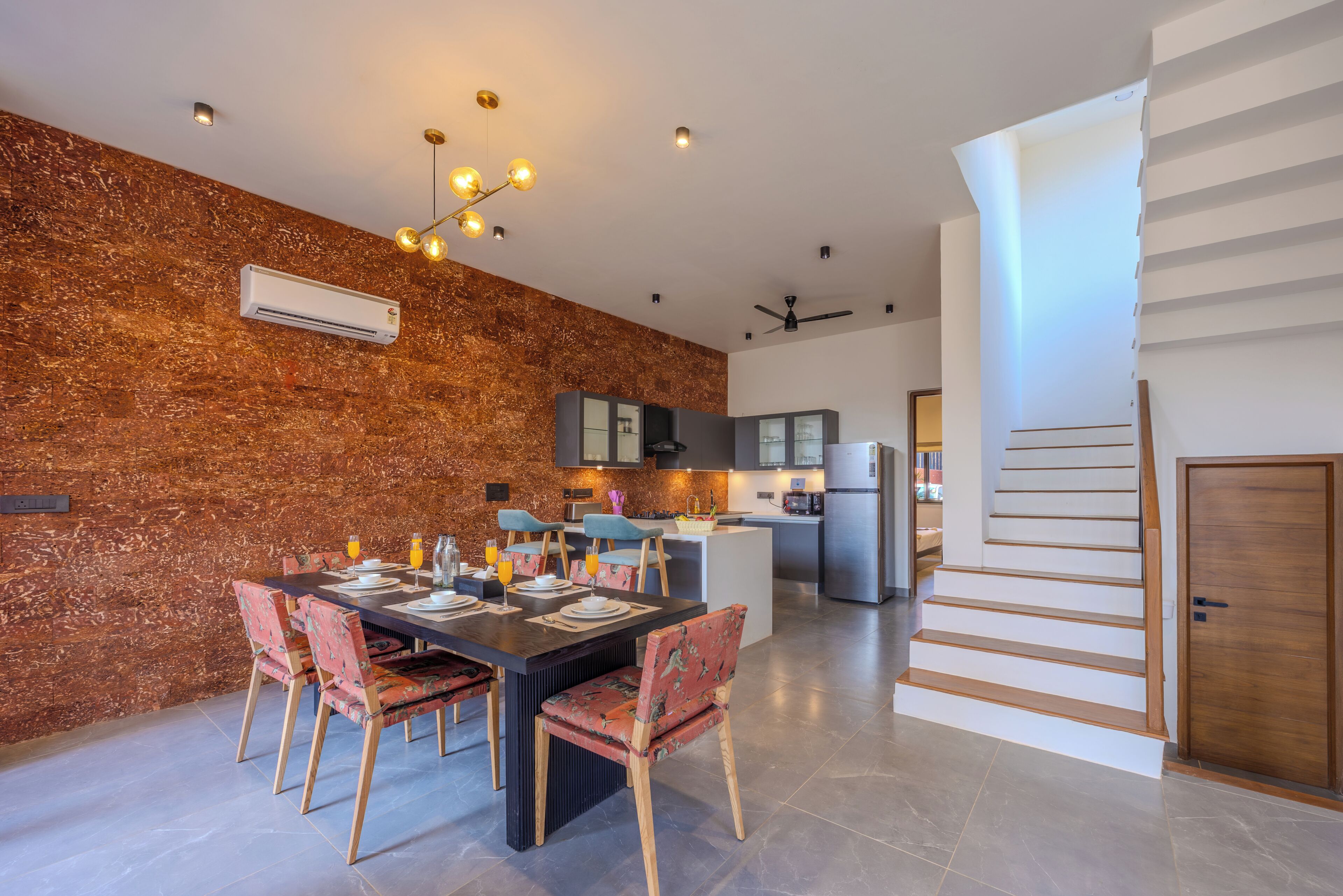 Uma cozinha moderna com uma ilha central, uma área de jantar com mesa e cadeiras, e uma escadaria que dá para outro andar.