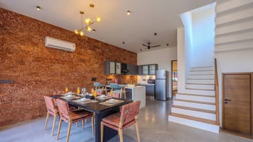 Uma cozinha moderna com uma ilha central, uma área de jantar com mesa e cadeiras, e uma escadaria que dá para outro andar.