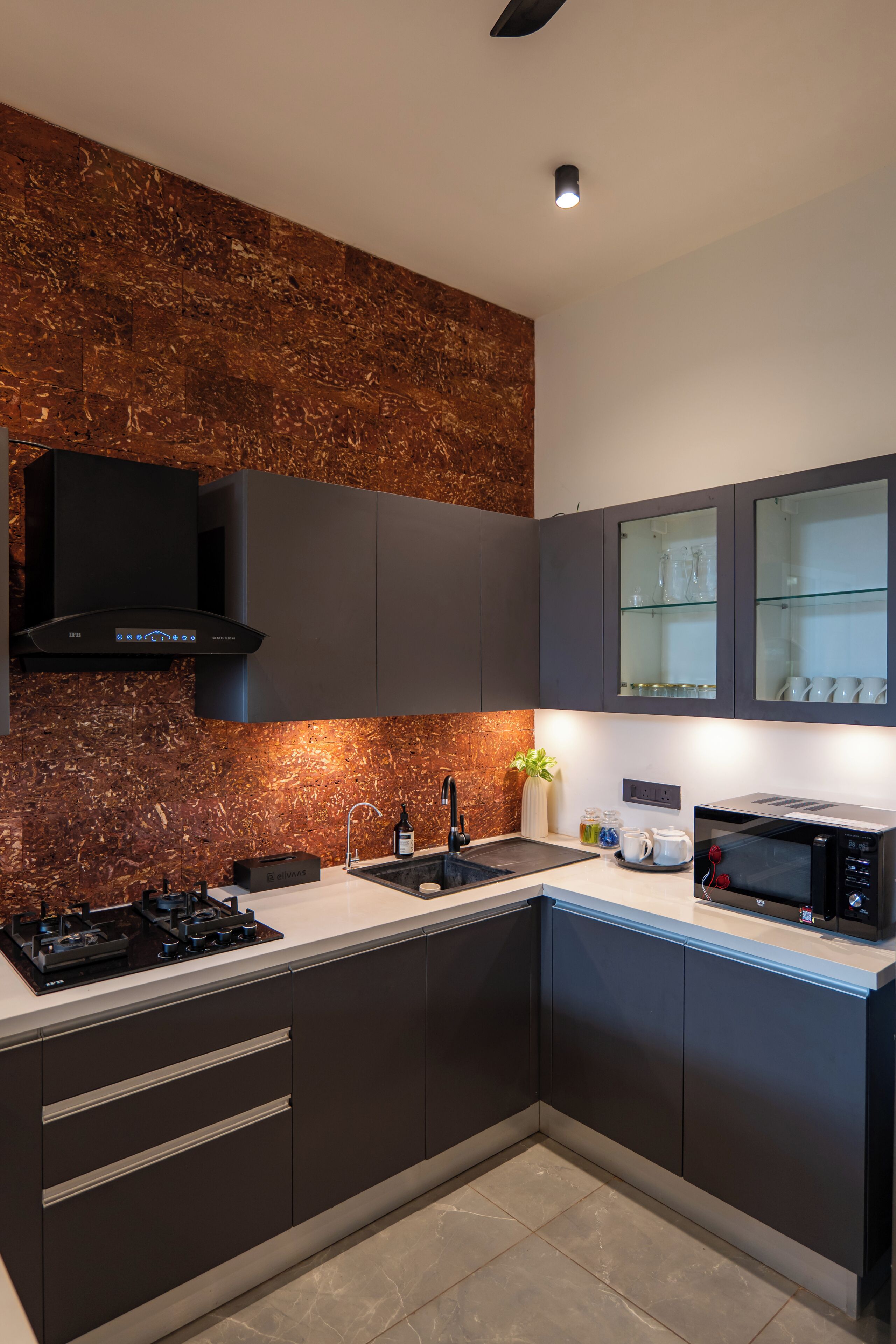 A modern kitchen with dark cabinetry, a stainless steel range hood, a built-in microwave, and a backsplash with a textured pattern.