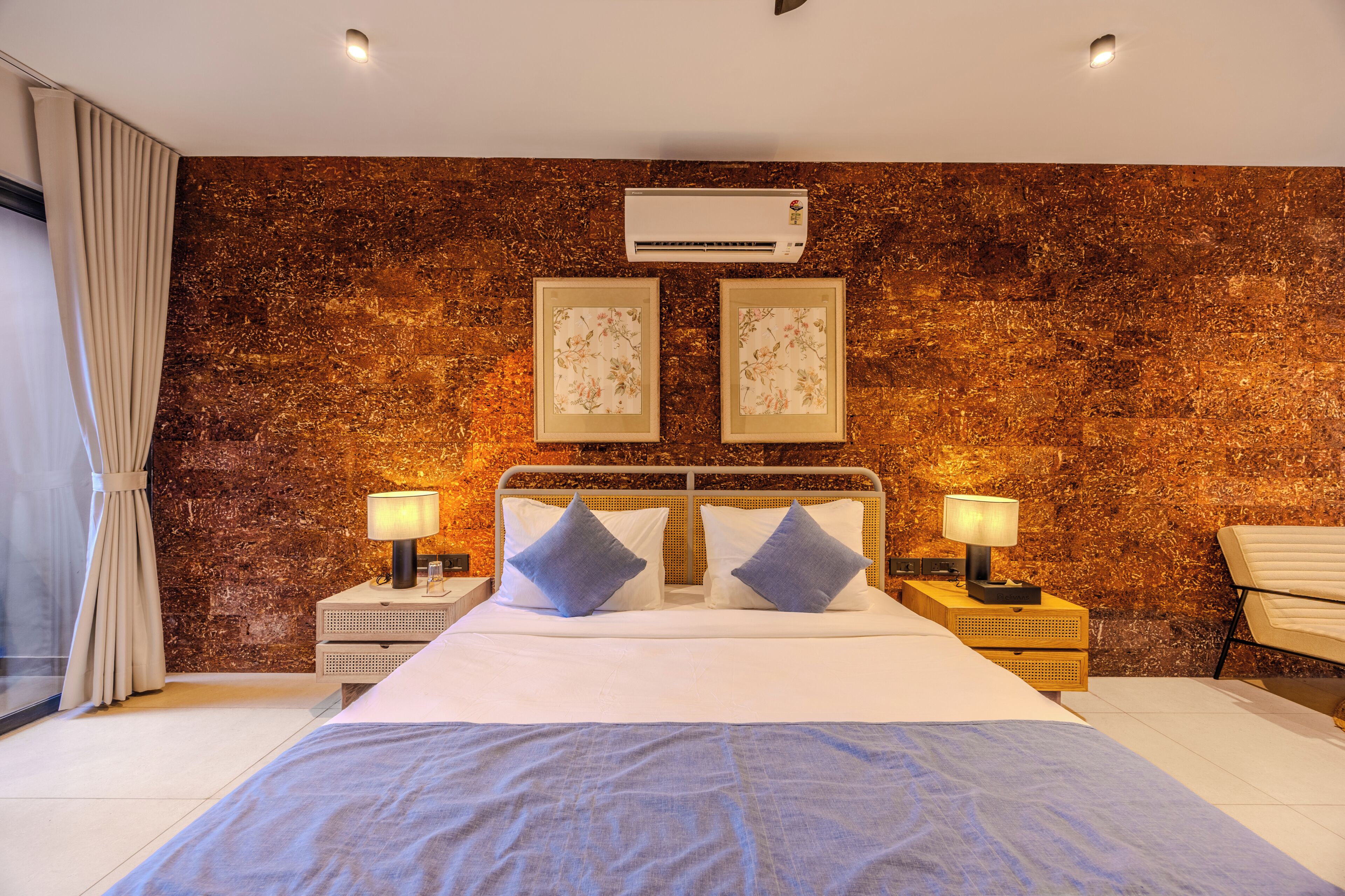A hotel room with a bed, two wall-mounted air conditioning units, a wooden textured wall, and two framed pictures.