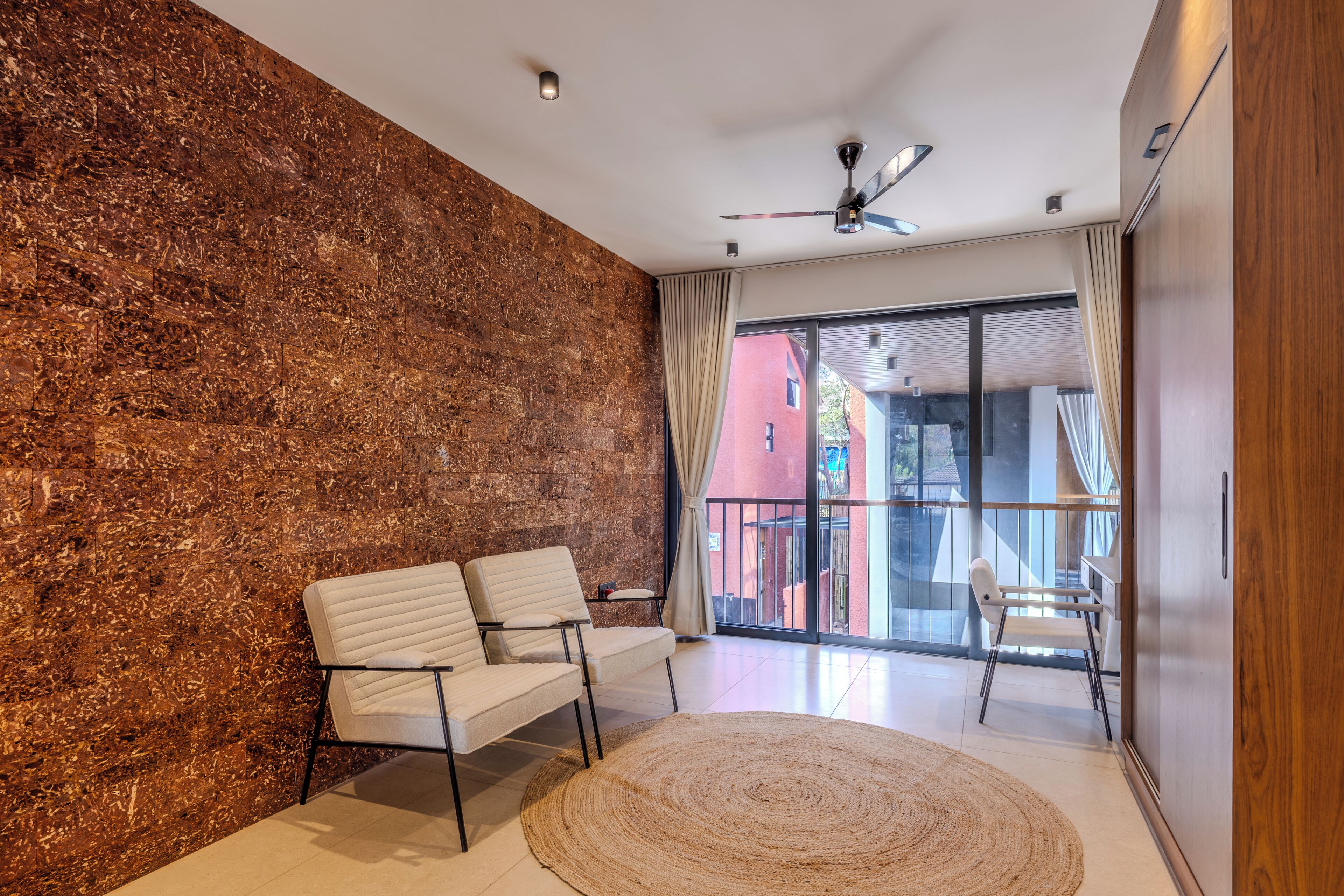 Ein modernes Wohnzimmer mit Steinwand, zwei weißen Sofas, einem großen Fenster und einem Deckenventilator.