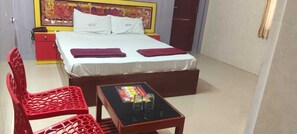 A hotel room with a bed, two red chairs, a small table with a card game, and a door.