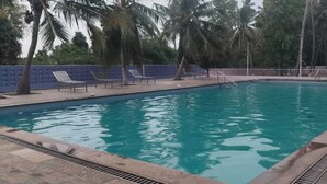 En swimmingpool med et blåt vandelement, omgivet af palmer og en stenvæg.