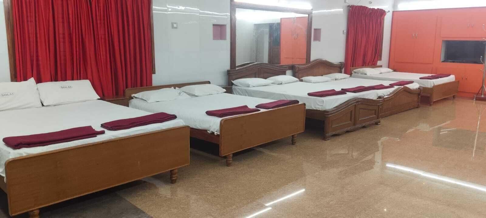 A hotel room with four wooden beds arranged in a row, each with white bedding and red towels.