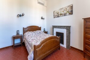 A bedroom with a wooden bed, a nightstand, a dresser, a fireplace, and a wall-mounted light fixture. - Spacious Holiday Home for 10 person (Saint-Laurent-la-Vernède)