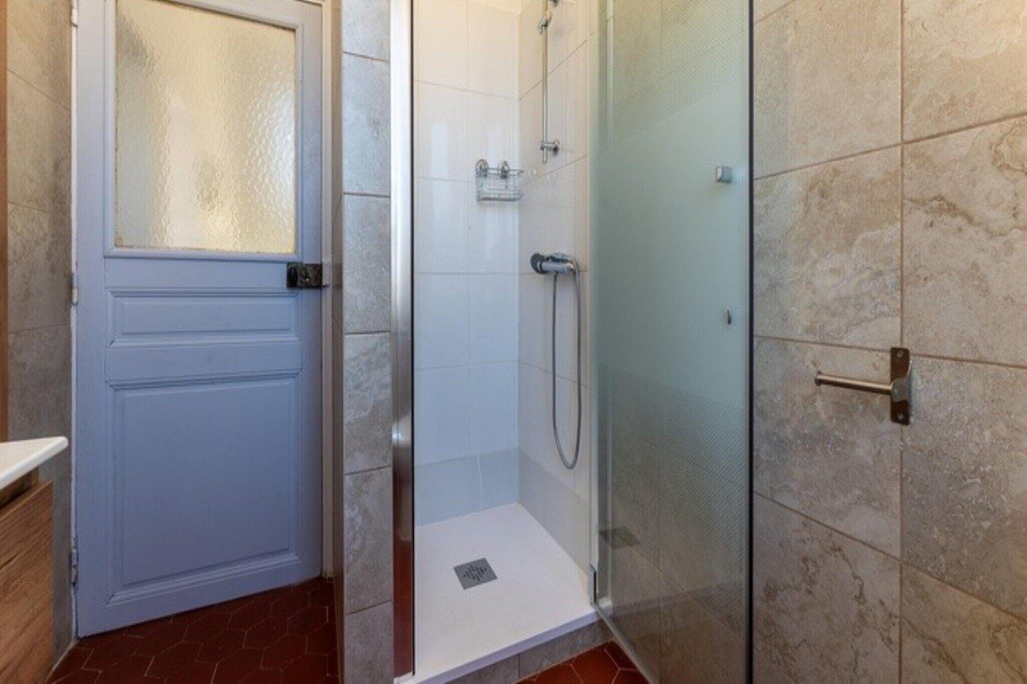 A bathroom with a glass shower enclosure, a white door with frosted glass, and tiled walls.